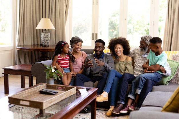 Famiglia di razza mista multigenerazionale che si gode il tempo a casa insieme, seduta su un divano, parlando, guardandosi l'un l'altro e sorridendo
