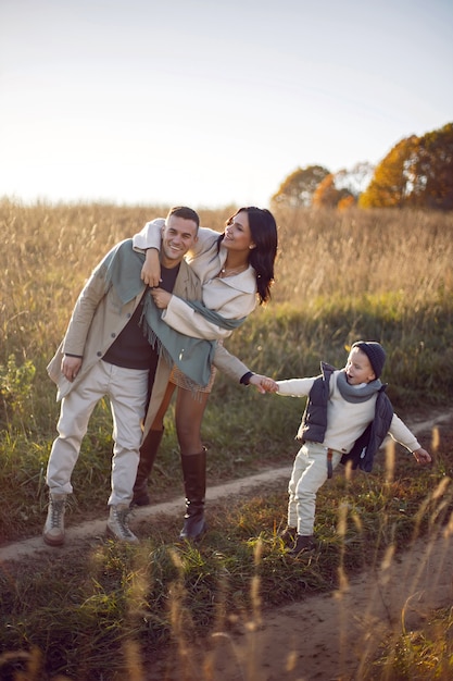 Famiglia di tre persone con un bambino mamma e papà sono in piedi su un campo in autunno al tramonto