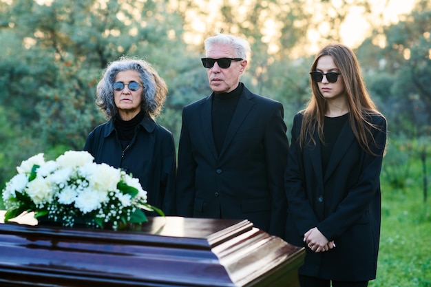 Famiglia di tre persone dal cuore spezzato in abiti da lutto e occhiali da sole