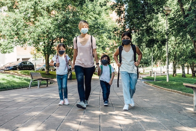 Famiglia di una madre con i suoi tre figli caucasici che vanno a scuola all'inizio dell'anno scolastico indossando maschere a causa della pandemia di coronavirus covid19
