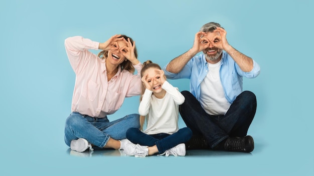 Famiglia divertendosi guardando attraverso il dito occhiali sfondo blu