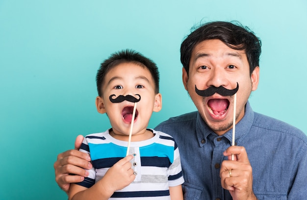 Famiglia divertente felice hipster padre e suo figlio bambino che tiene i baffi neri puntelli