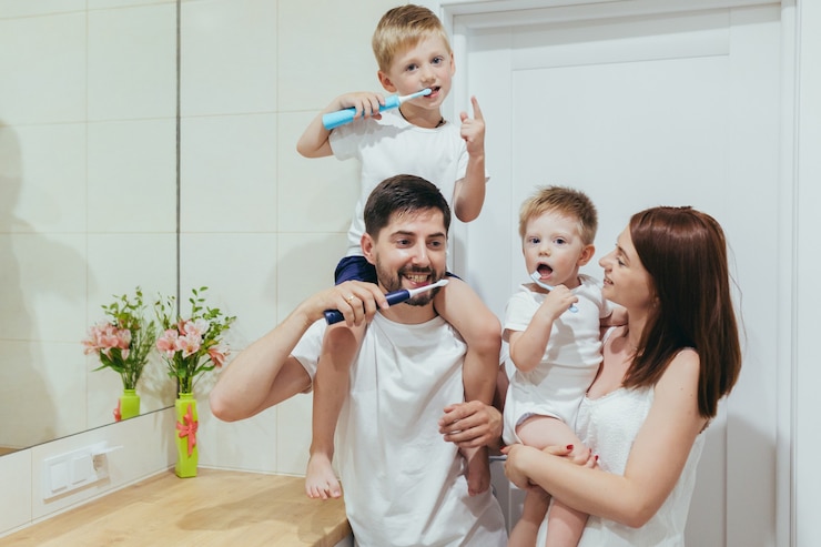 Foto famiglia, due adulti e due bambini piccoli si lavano i denti insieme in bagno