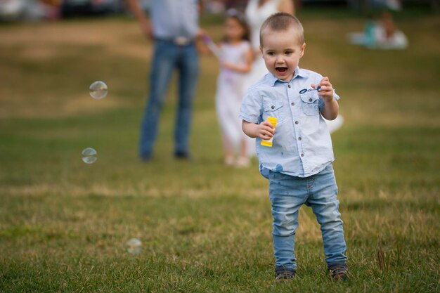 Famiglia durante la passeggiata nel parco ragazzino che soffia bolle di sapone teleobiettivo