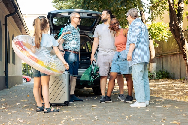 Famiglia e amici diversi che viaggiano in vacanza al mare, andando in auto con bagagli e valigia. Bambino, genitori e nonni in partenza per le vacanze estive con bagaglio e gommone.