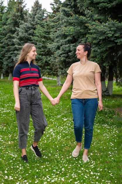 Famiglia e concetto di svago. Madre e figlia sorridenti felici che tengono le mani e che camminano nel parco