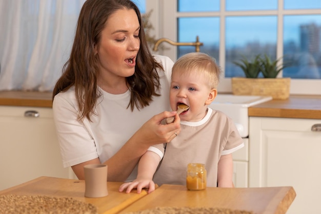 Famiglia felice a casa madre che allatta il suo bambino dal cucchiaio in cucina piccolo bambino con mes