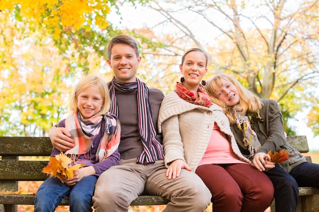 Famiglia felice all&#39;aperto seduti sulla panchina in autunno