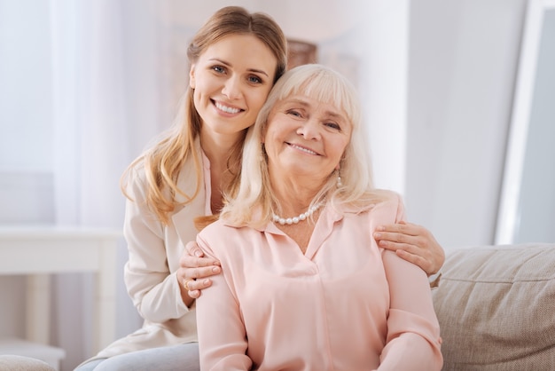 Famiglia felice. Bella giovane donna positiva che sorride e ti guarda mentre abbraccia sua madre