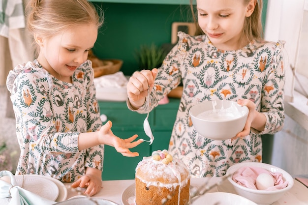 Famiglia felice candido bambini sorelle ragazze insieme si divertono vacanze di Pasqua primaverili pronte a casa in cucina che decorano la tavola e torte pasquali da forno glassa dolce e caramelle per pranzo o cena