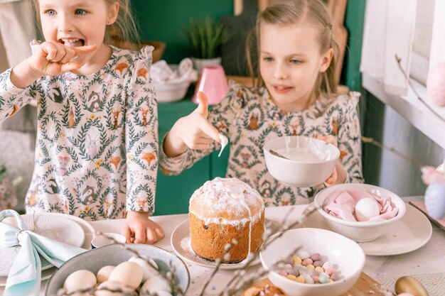 Famiglia felice candido bambini sorelle ragazze insieme si divertono vacanze di Pasqua primaverili pronte a casa in cucina che decorano la tavola e torte pasquali da forno glassa dolce e caramelle per pranzo o cena