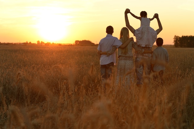 Famiglia felice che cammina nel campo e guarda il tramonto