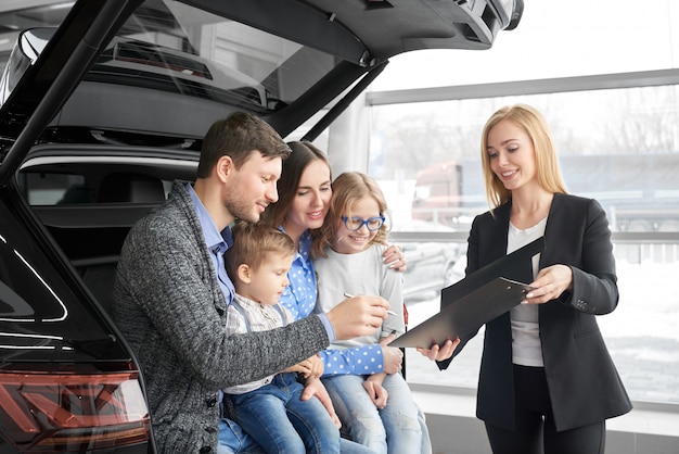 Famiglia felice che compra nuova automobile nera comoda nel salone automatico