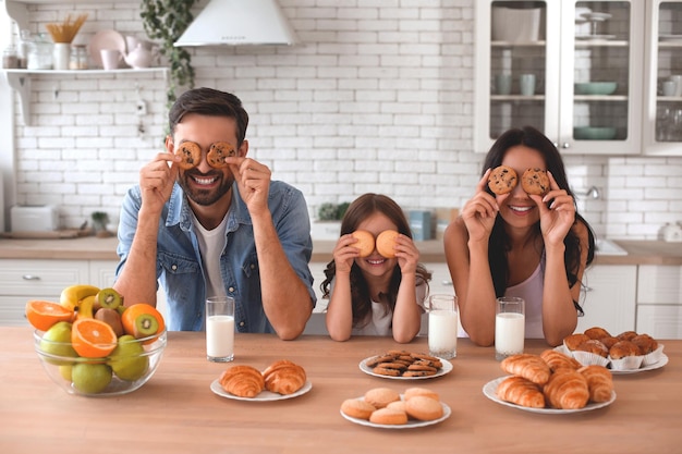 Famiglia felice che copre gli occhi con i biscotti in cucina