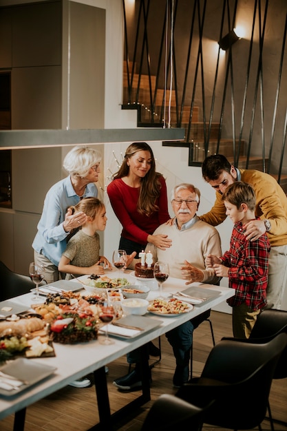 Famiglia felice che festeggia il compleanno del nonno con torta e candele a casa