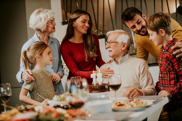 Famiglia felice che festeggia il compleanno del nonno con torta e candele a casa