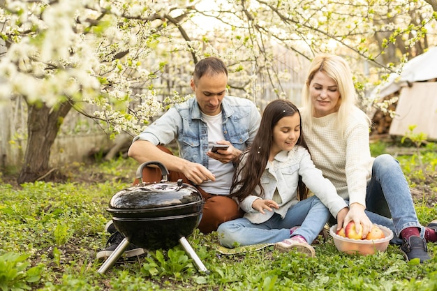 Famiglia felice che ha un barbecue nel loro giardino in primavera. Concetto di tempo libero, cibo, famiglia e vacanze.