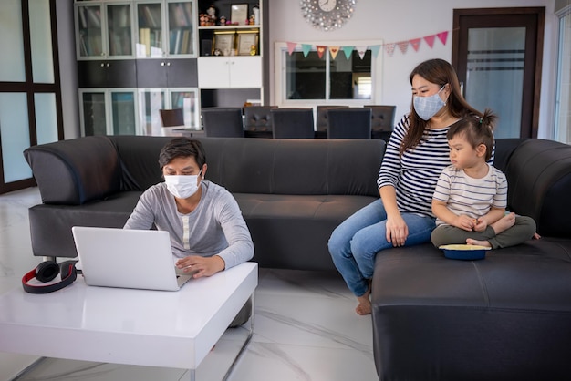 Famiglia felice che indossa una maschera per il viso Giovane padre che lavora lavora da casa mentre fa da babysitter a sua figlia