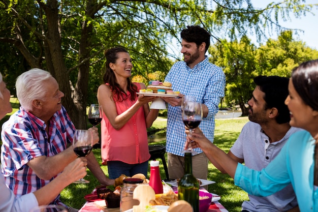 Famiglia felice che mangia i bigné e vino rosso in parco