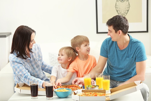 Famiglia felice che mangia pizza sul divano tutti insieme