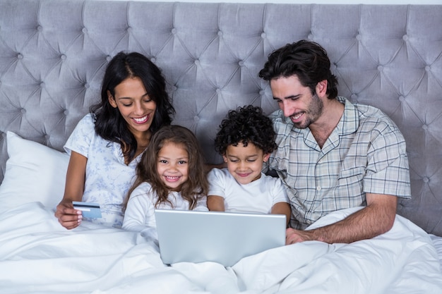 Famiglia felice che per mezzo del computer portatile sul letto