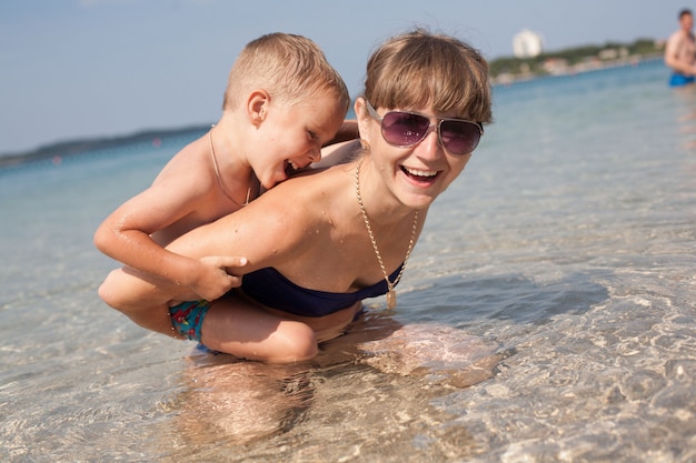 Famiglia felice che riposa sulla costa di mare Croazia. giovane madre nuota e gioca con il figlio sulla riva del mare. ricreazione all'aperto attiva. fine settimana estivo in croazia. donna sorridente con ragazzino gioca sulla spiaggia