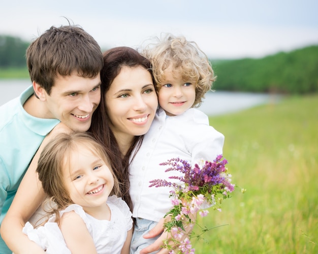 Famiglia felice che si diverte all'aperto nel campo primaverile contro erba sfocata e sfondo del cielo