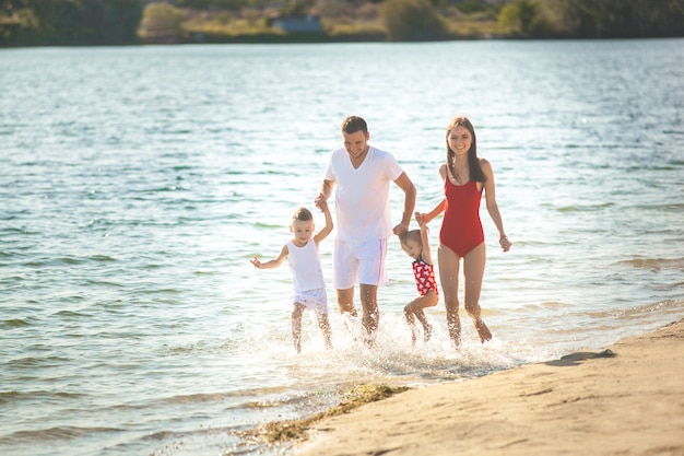 Famiglia felice che si diverte in spiaggia. Mamma, papà, figlio e figlia piccola in riva al mare. Famiglia allegra