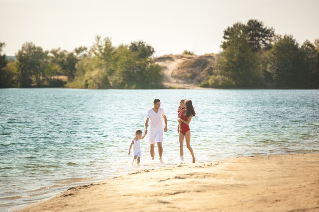 Famiglia felice che si diverte in spiaggia. Mamma, papà, figlio e figlia piccola in riva al mare. Famiglia allegra