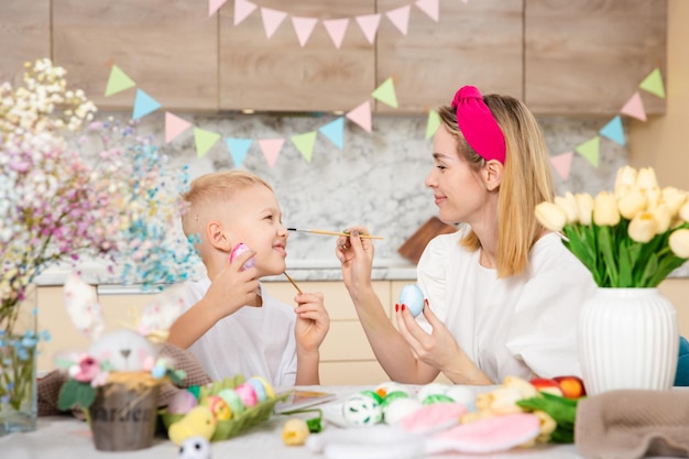 Famiglia felice che si prepara per la Pasqua Bambino carino con la madre che dipinge le uova Attività domestica Concetto di unità e amore Mamma e figlio