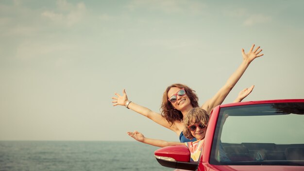 Famiglia felice che si rilassa sulla spiaggia Donna e bambino che si divertono in cabriolet rosso contro il cielo blu Vacanze estive e concetto di viaggio