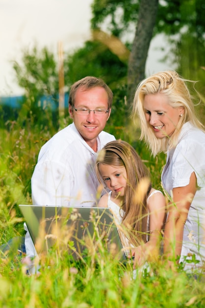 Famiglia felice che si siede nel prato con il computer portatile