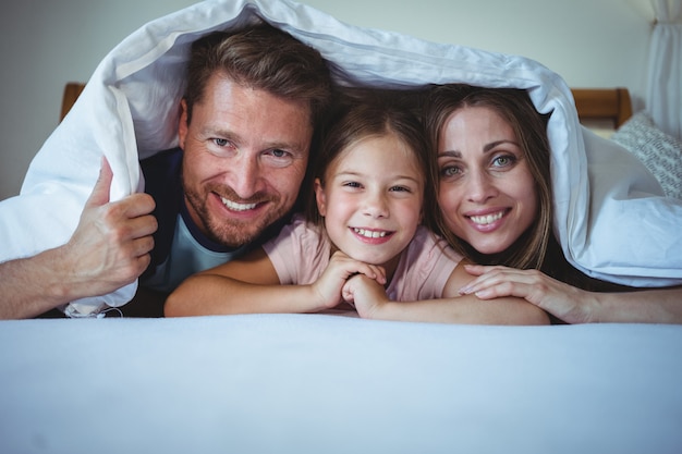 Famiglia felice che si trova sotto una coperta sul letto
