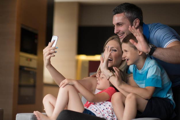 Famiglia felice che si trova sul divano e utilizza il cellulare per la videochiamata a casa