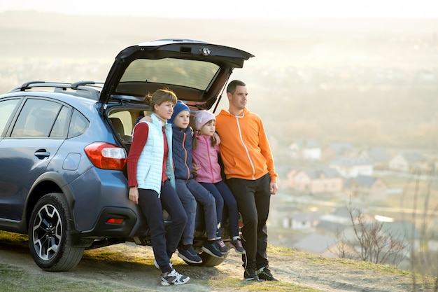 Famiglia felice che sta insieme vicino ad un'automobile con il tronco aperto che gode della vista