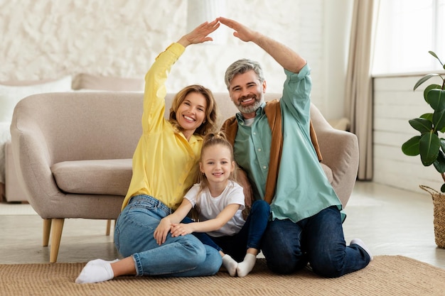 Famiglia felice che unisce le braccia come un tetto seduto a casa