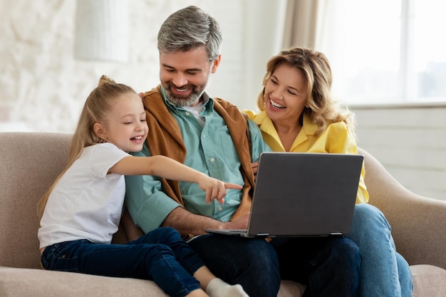 Famiglia felice che utilizza il computer portatile che naviga in internet seduto sul divano all'interno