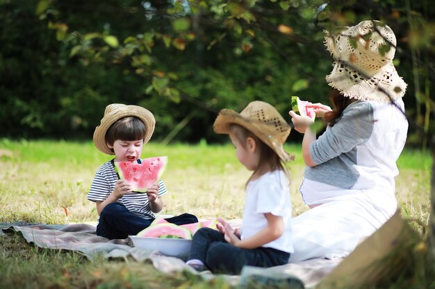 Famiglia felice con bambini che fanno picnic nel parco genitori con bambini seduti sull'erba del giardino e che mangiano anguria all'aperto