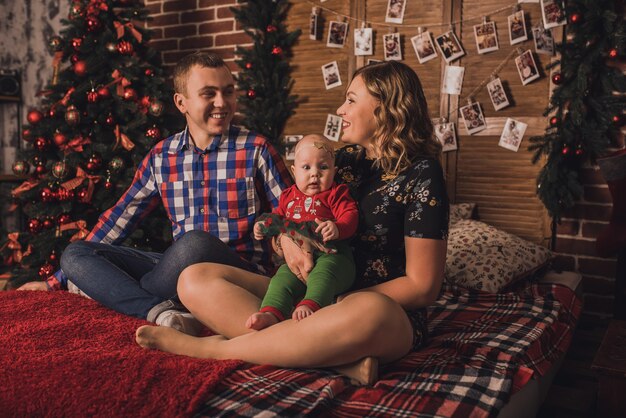 Famiglia felice con bambino che celebra il nuovo anno e il Natale all'albero di Natale decorato e alle ghirlande
