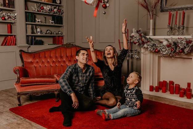 Famiglia felice con bambino che celebra il nuovo anno e il Natale all'albero di Natale decorato e alle ghirlande