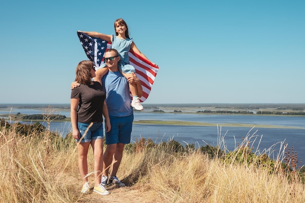 Famiglia felice con bandiera americana che si gode la natura in una soleggiata giornata estiva Stile di vita libero