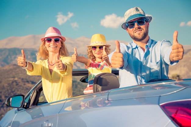 Famiglia felice con cappelli colorati sul tetto dell'auto convertibile che fa segno ok con sfondo di montagna