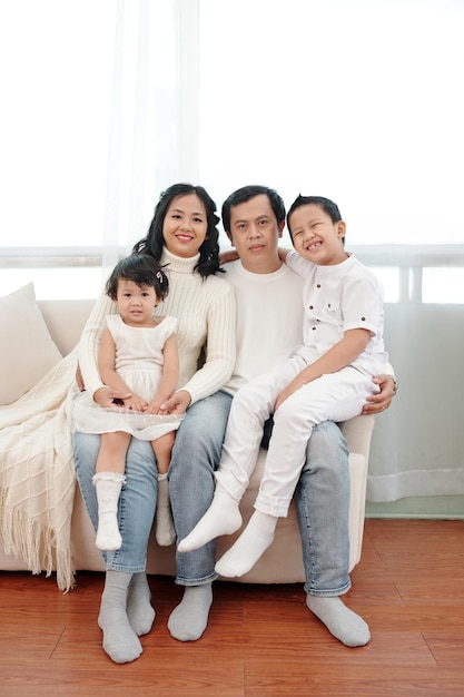 Famiglia felice con due bambini seduti sul divano di casa e guardando la telecamera