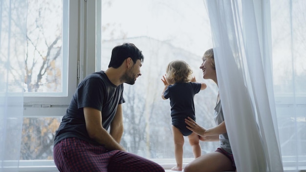 Famiglia felice con giovane figlia carina seduta sul davanzale che gioca e guarda nella finestra a casa