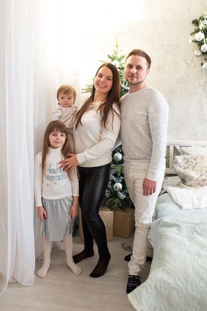 Famiglia felice con il bambino in piedi vicino all'albero di Natale a casa