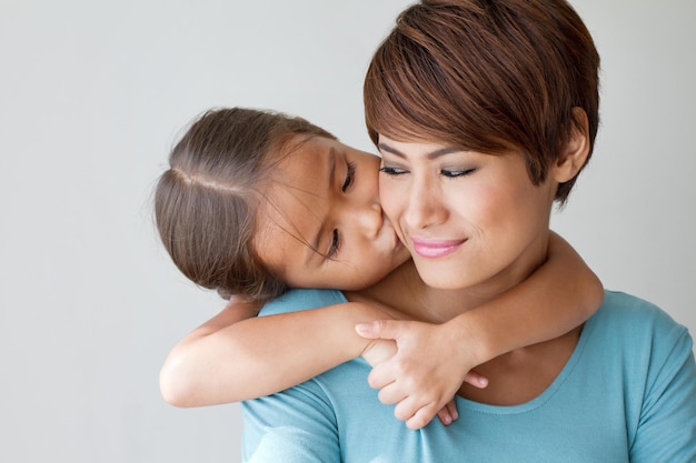 Famiglia felice con la figlia positiva sorridente che bacia la guancia di sua madre