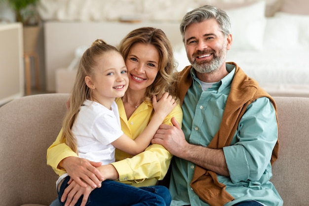 Famiglia felice con la piccola figlia che posa abbracciando a casa