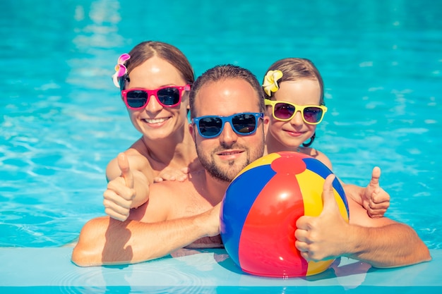 Famiglia felice con occhiali da sole e fiori sui capelli facendo un gesto ok all'interno della piscina