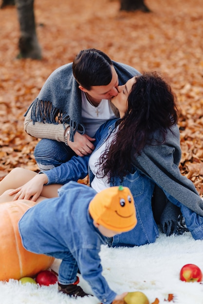 Famiglia felice con piccolo bambino sveglio nel parco sulla foglia gialla con grande zucca in autunno