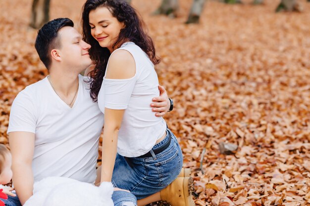 Famiglia felice con piccolo bambino sveglio nel parco sulla foglia gialla con grande zucca in autunno